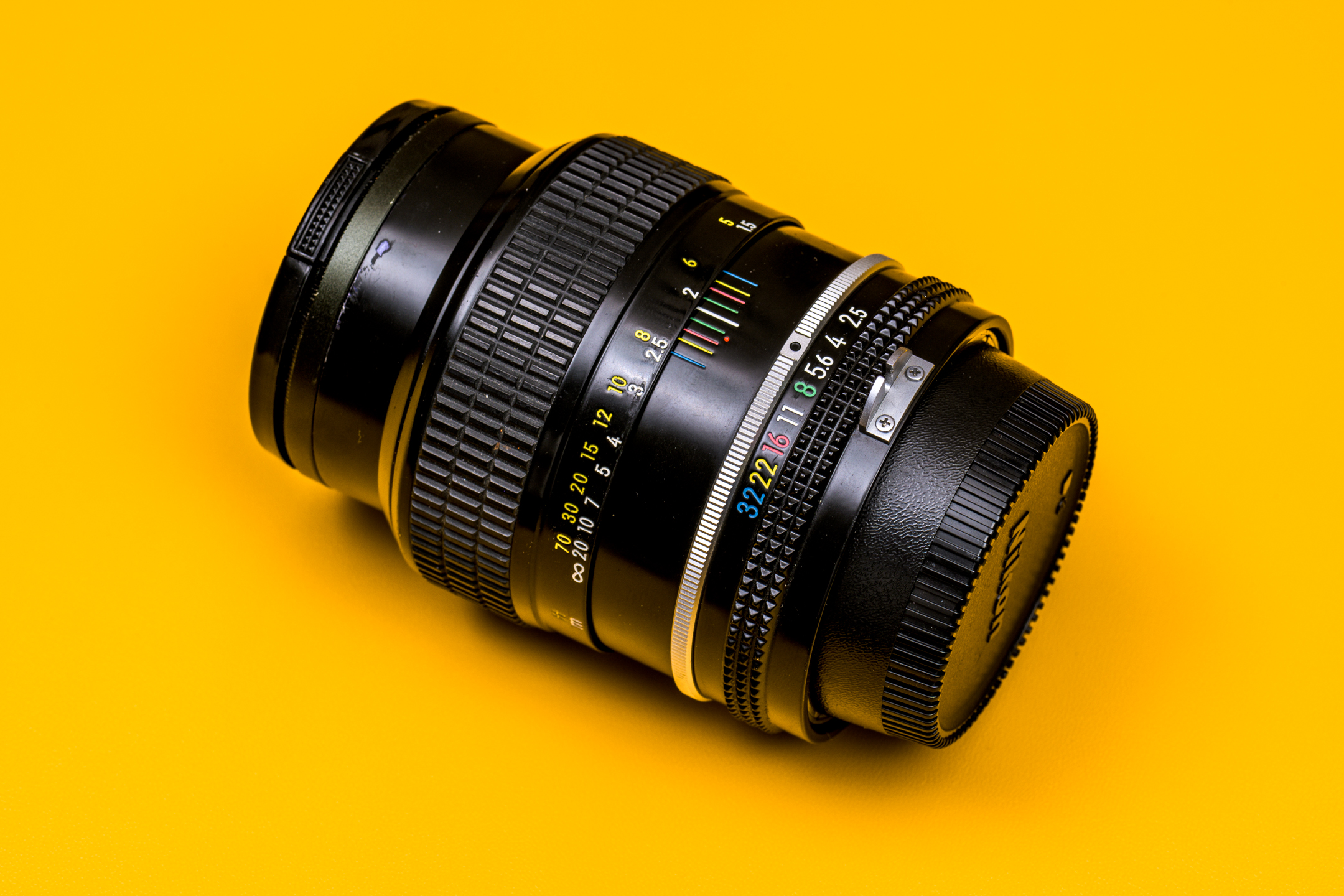 De Nikkor 105m f/2.5 K, een vintage fotografie-objectief, op een gele achtergrond.