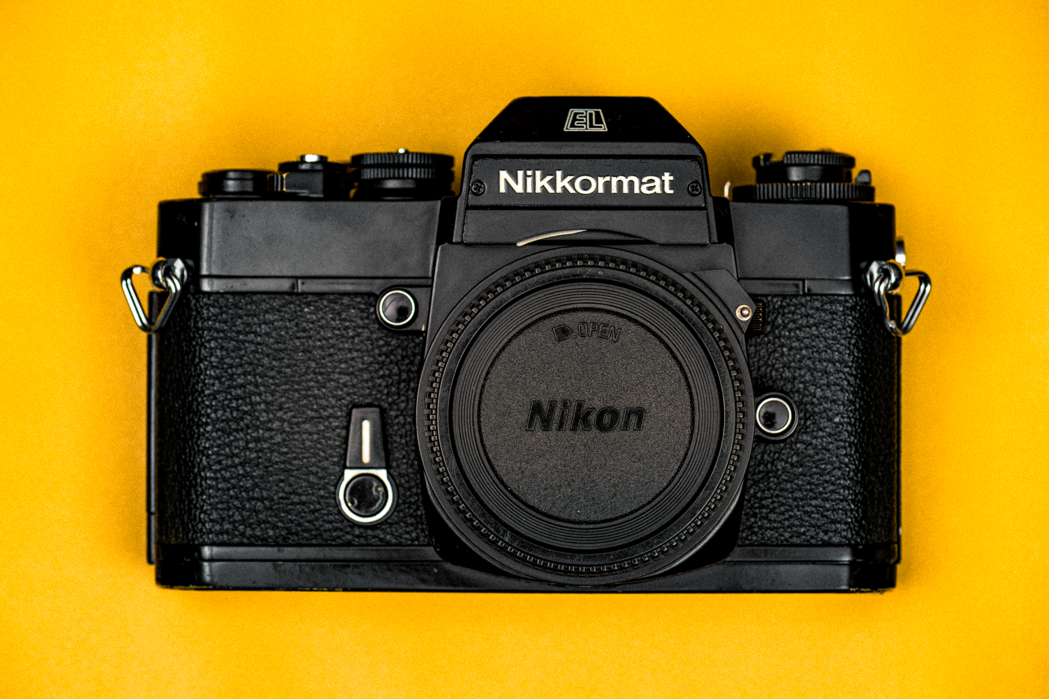 Bovenaanzicht van een zwarte Nikkormat EL-camera, op een Nikon-gele achtergrond.