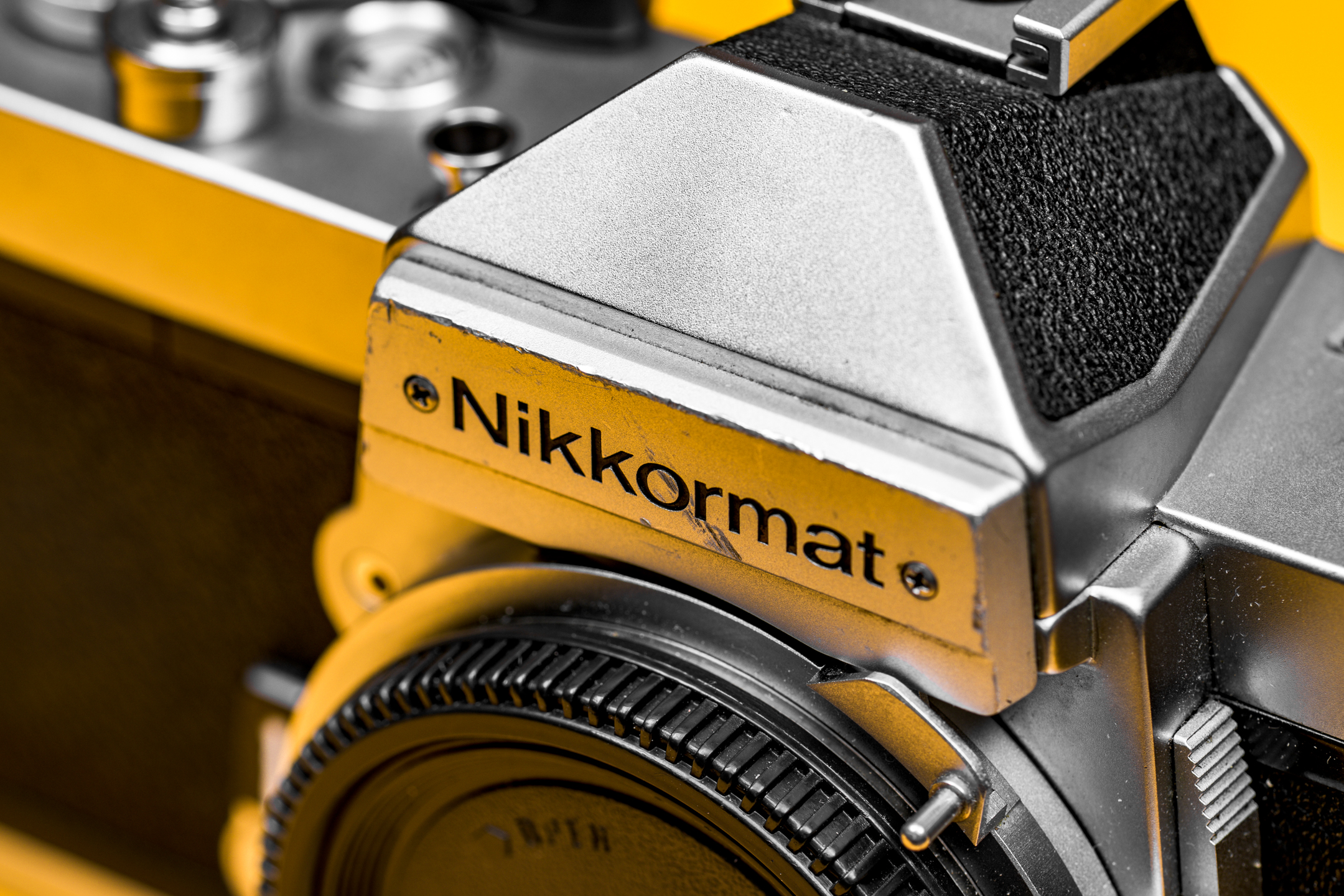 Close-up van het beeldmerk op een Nikkormat FT2; er zit een flinke kras op het metalen plaatje. De achtergrond kleurt een Nikon-achtig geel.
