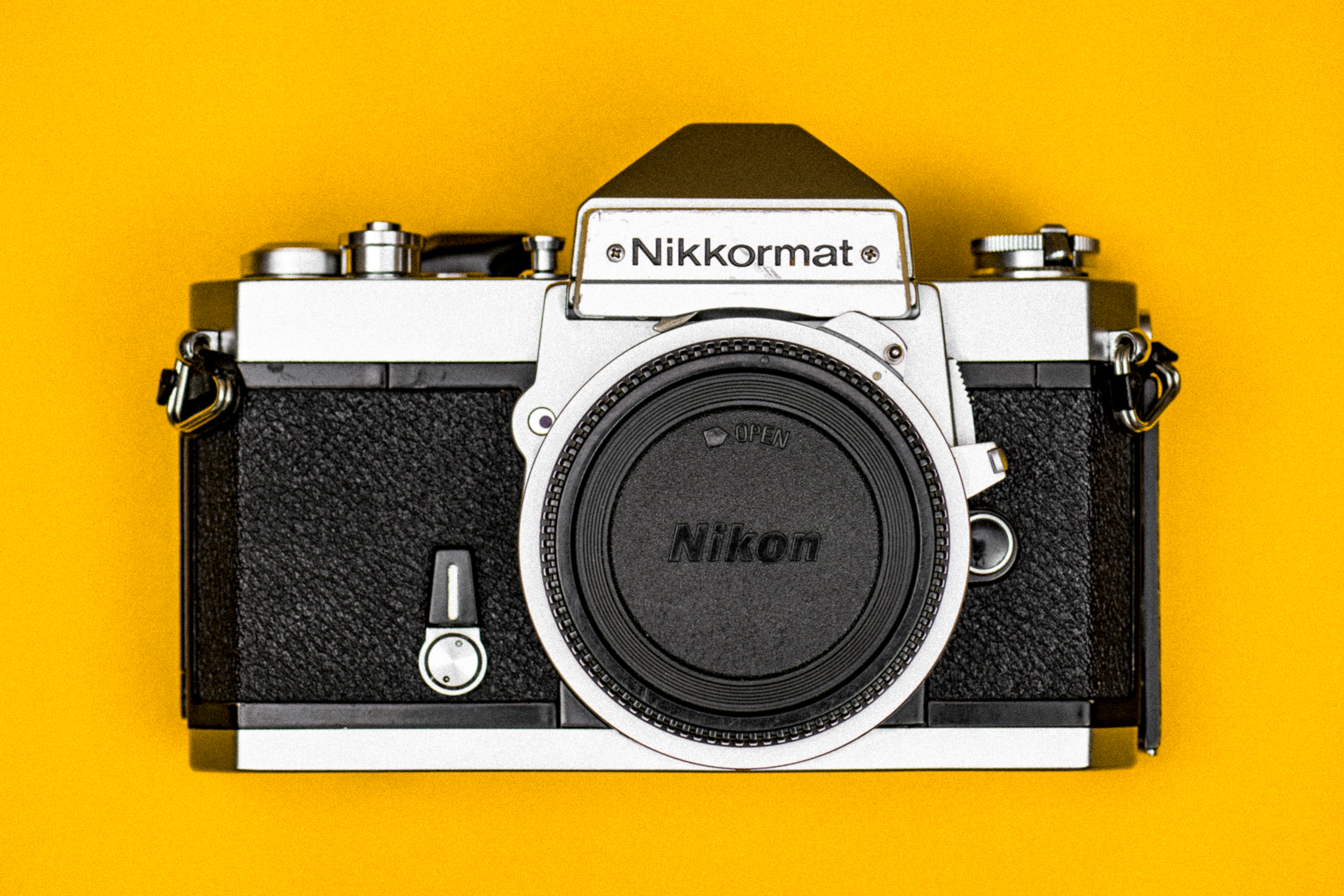 Bovenaanzicht van een zilverkleurige Nikkormat FT2-camera, op een Nikon-gele achtergrond.